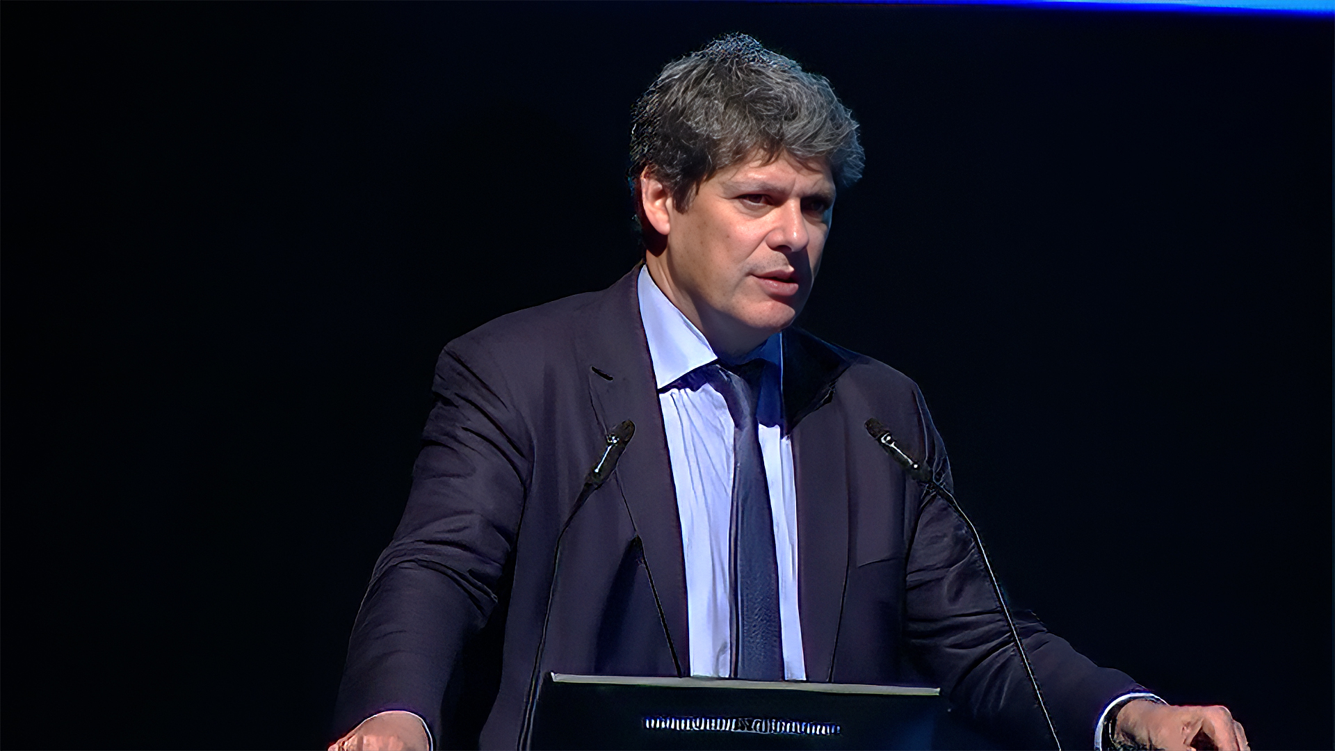 Man standing at podium explaining concepts to a live audience.